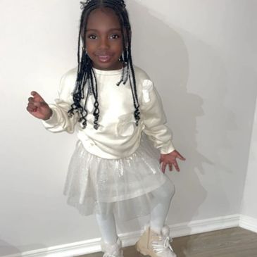 A young girl wearing a cream sweatshirt and sparkly tutu stands smiling beneath the Journeesky logo 