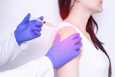 A healthcare professional wearing gloves administers a vaccine injection to a woman's upper arm.
