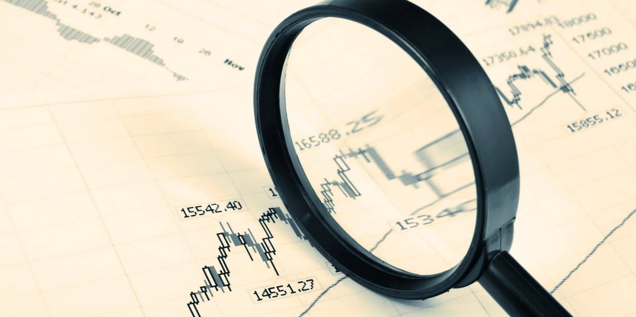 Magnifying glass over financial charts showing stock market trends and numbers.