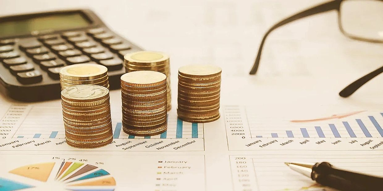 Stacks of coins on financial charts with a calculator and glasses.