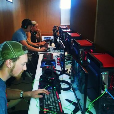 Group of young people gaming intensely on desktop computers in a dim room.