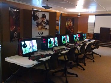 Gaming setup with multiple PCs and Overwatch posters.