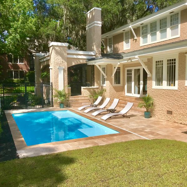 Backyard pool with lounge chairs beside a peach-colored house.