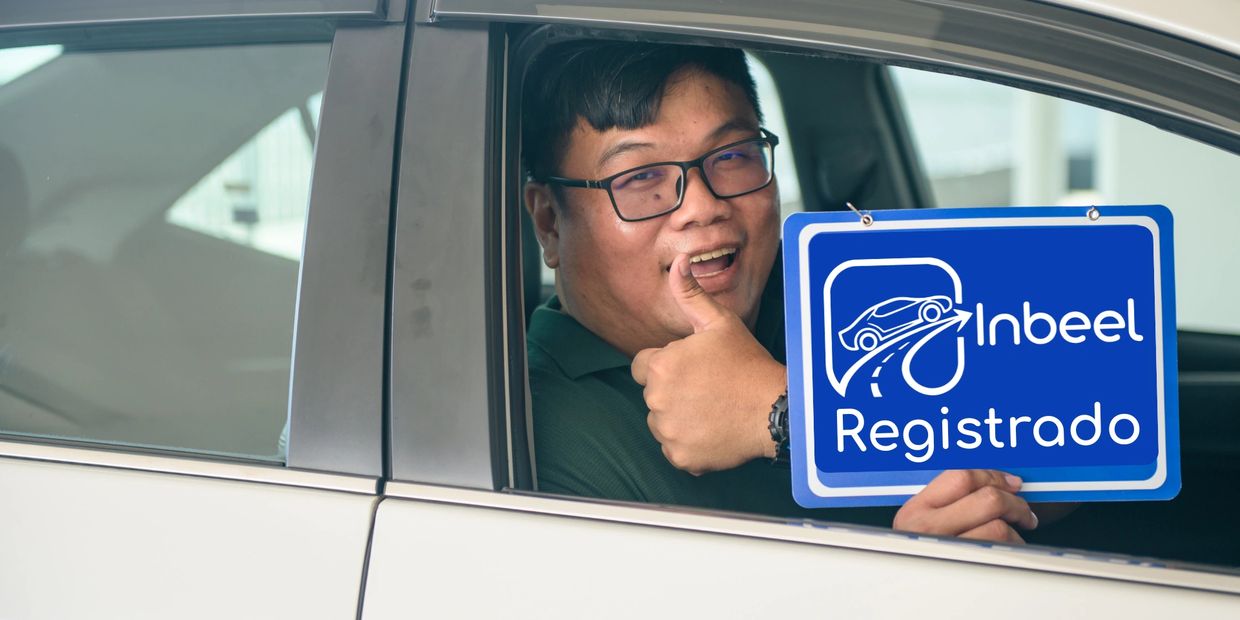Hombre sonriente con gafas muestra un cartel azul desde un coche.