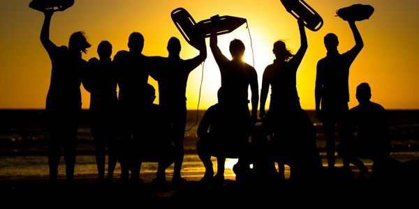 Silhouetted group holding surfboards at sunset on the beach.