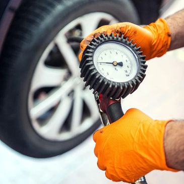 Person wearing orange gloves checking tire pressure with a gauge.