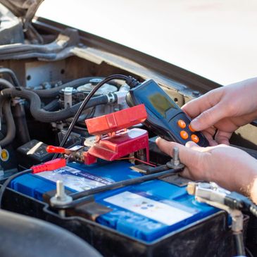 Person testing a car battery with a diagnostic tool under the hood.