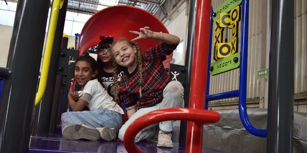 Three children smiling and posing inside a playground slide.
