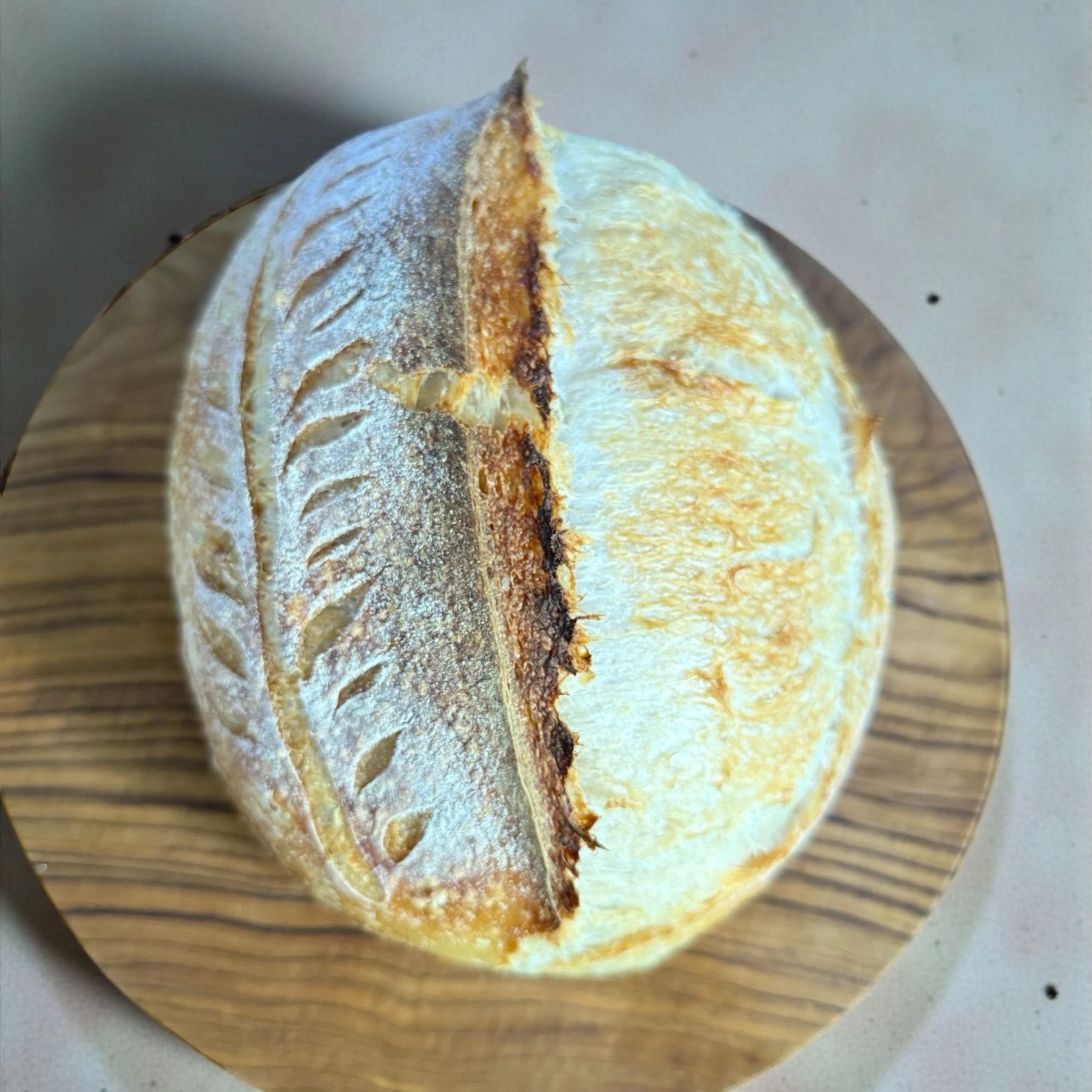 Round loaf of artisan bread with detailed scoring on a wooden board.