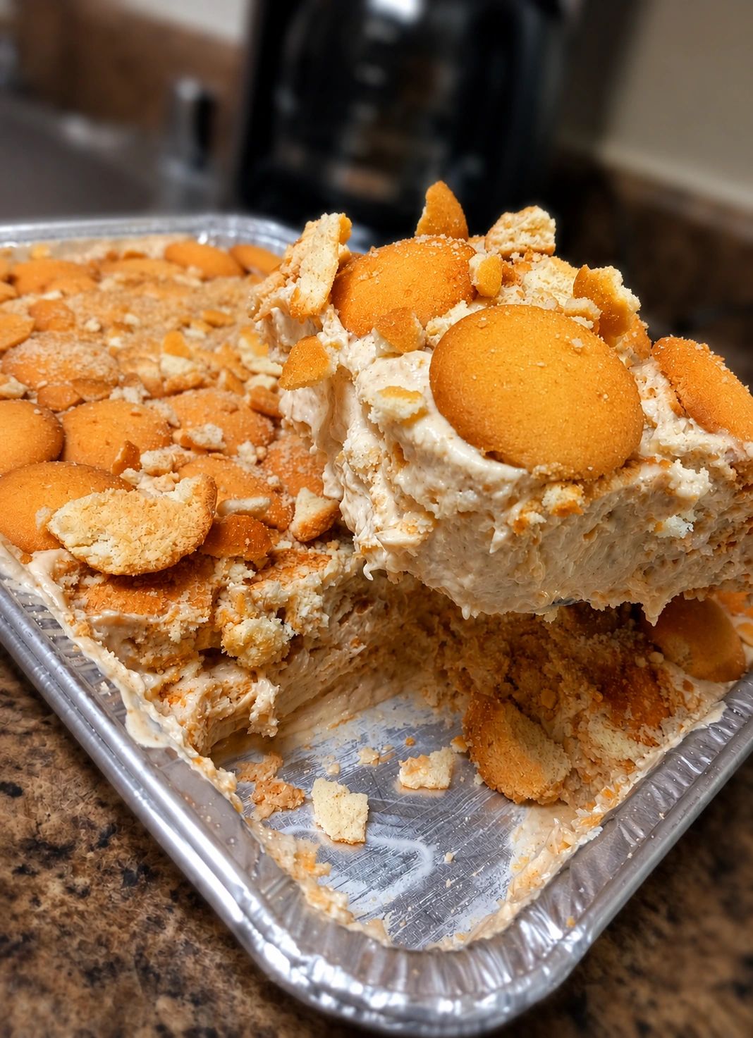 A creamy dessert topped with whole and crushed vanilla wafers in a foil tray.