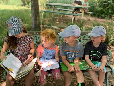 Four children sitting on a bench, reading books outdoors.