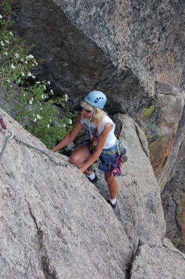 Woman rock climbing with safety gear on granite surface.
