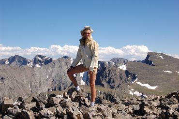 Person standing on rocky mountain peak with scenic backdrop.