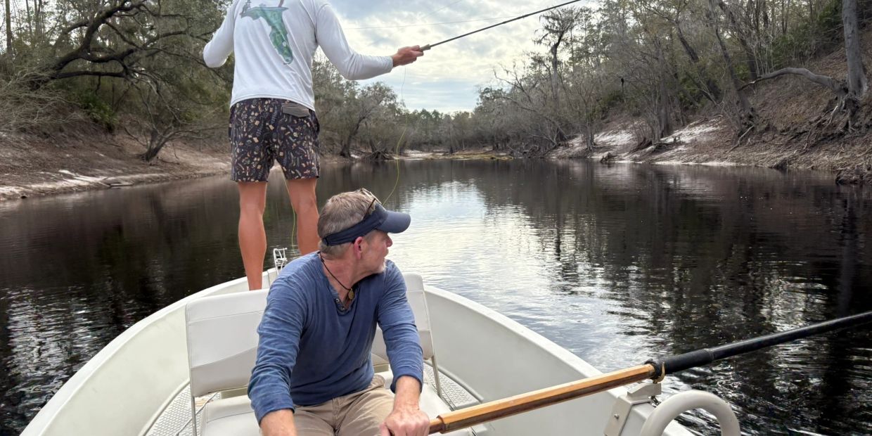 Two men fishing from a small boat on a calm river.