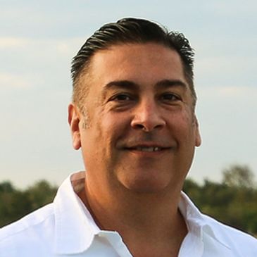 Smiling man in white shirt outdoors with a natural background.