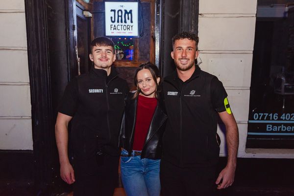 Two security guards and a woman posing outside The Jam Factory bar.