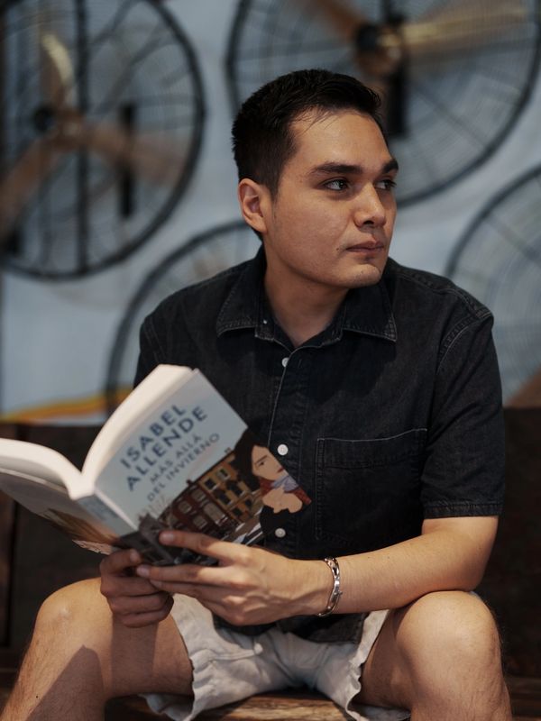 Young man reading a book by Isabel Allende in a modern setting.