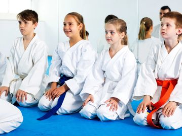Kids in karate uniforms sitting on mat.