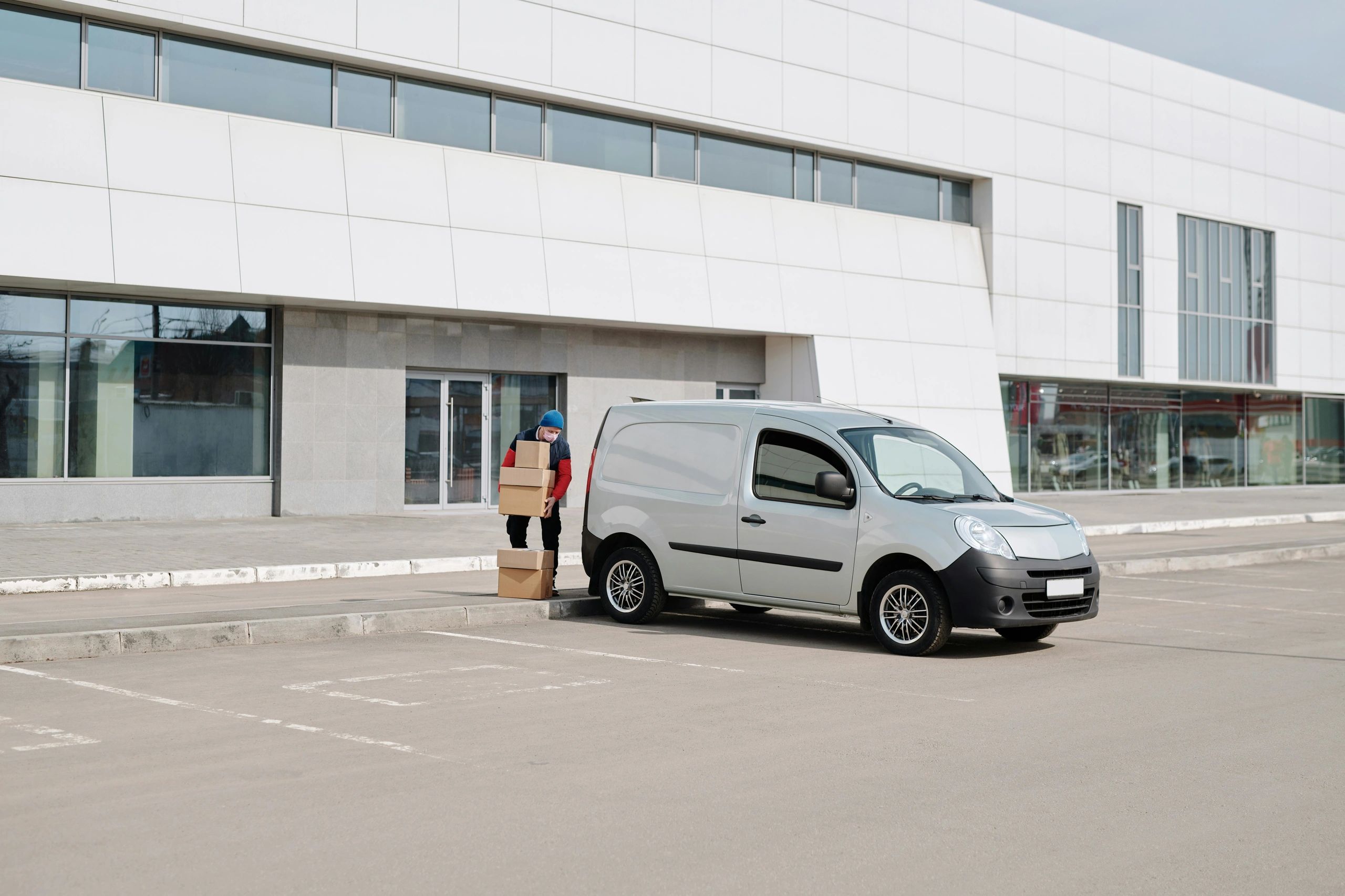 Delivery person unloading packages from a van in front of a modern building.