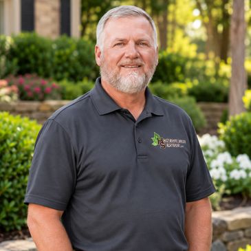 Smiling man in a dark polo shirt outdoors.