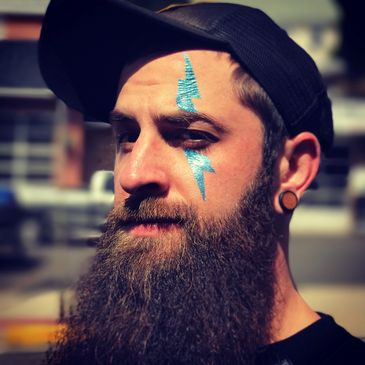Bearded man with blue lightning bolt face paint and a black cap.