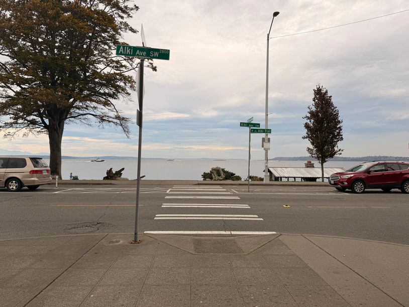 Crosswalk leading to a scenic waterfront with parked cars and street signs.