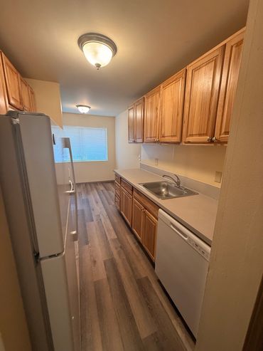 Clean, narrow kitchen with wooden cabinets and laminate flooring.