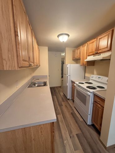 Narrow kitchen with wooden cabinets and white appliances.