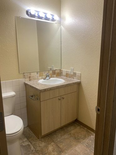 Small bathroom with a wooden vanity, white sink, and a toilet.