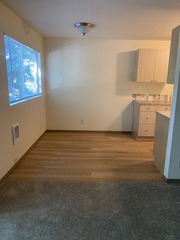 Empty kitchen dining area with wood flooring and window light.