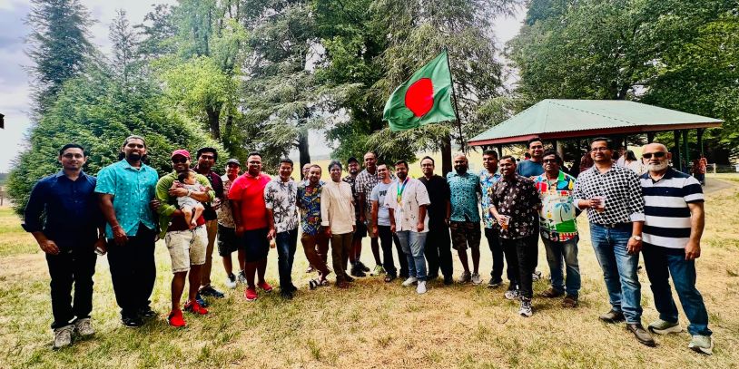 Group of people posing with Bangladesh flag outdoors.