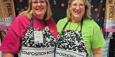 Two women wearing matching black and white aprons, smiling.