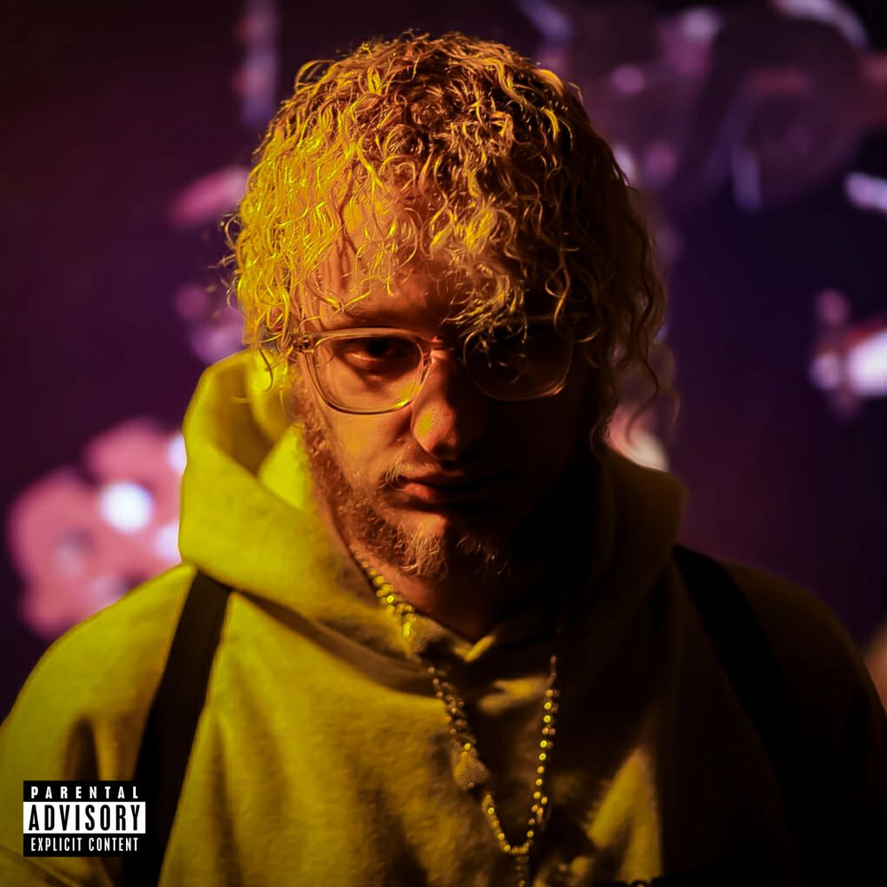 Portrait of a man with curly hair and glasses in moody lighting.