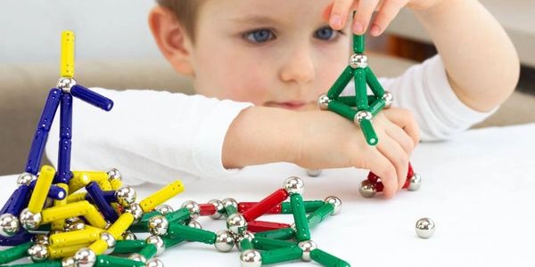 A child plays with colorful magnetic building sticks and metal balls.