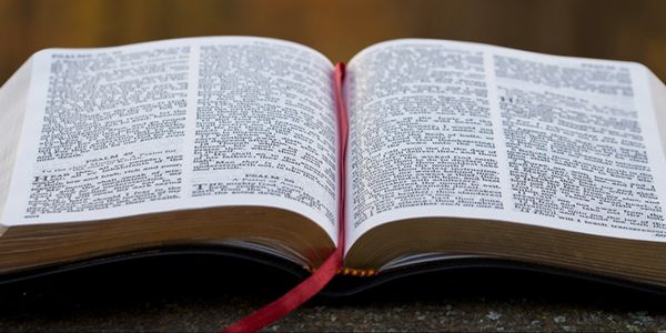 Open Bible with red ribbon bookmark on a wooden surface.