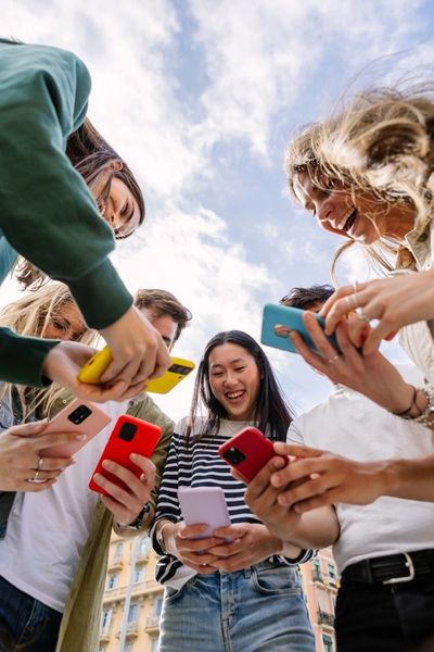 Group of friends happily looking at their smartphones outdoors.