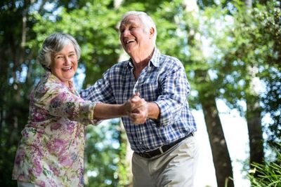 Elderly couple joyfully dancing outdoors in a lush green setting.