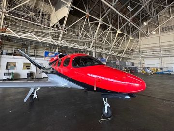 A sleek red and black small aircraft inside a spacious hangar.