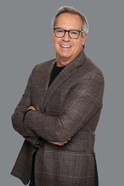 Smiling man in glasses and checkered blazer.
