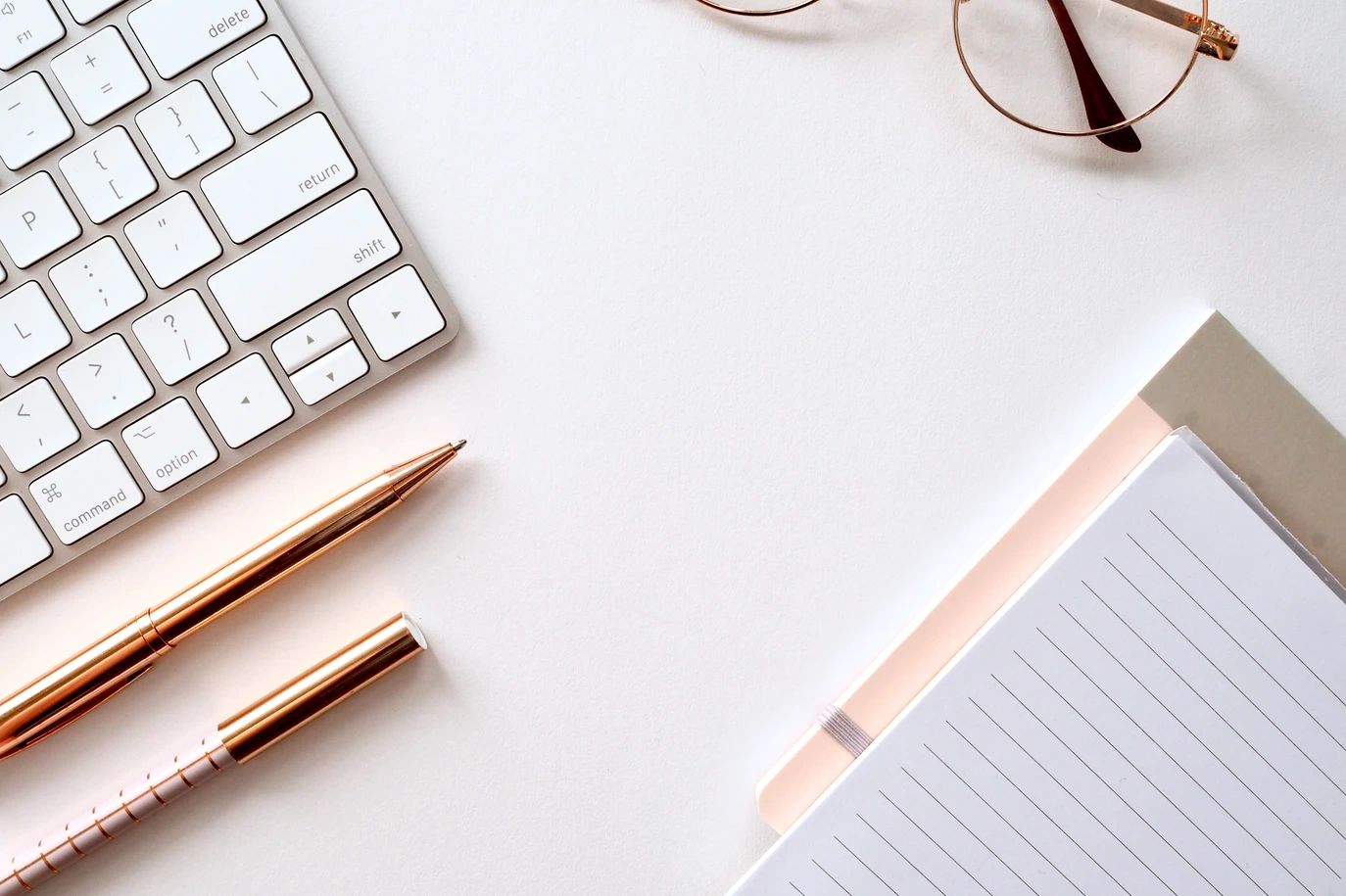 Workspace with keyboard, pens, glasses, and notebook.