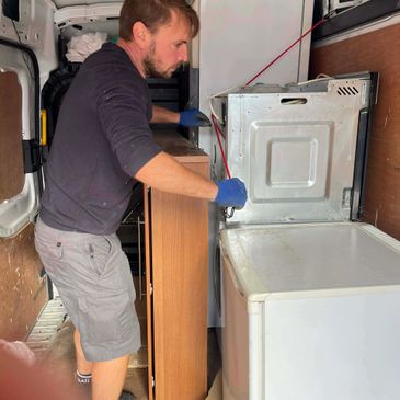 Man repairing an appliance inside a van, wearing gloves.