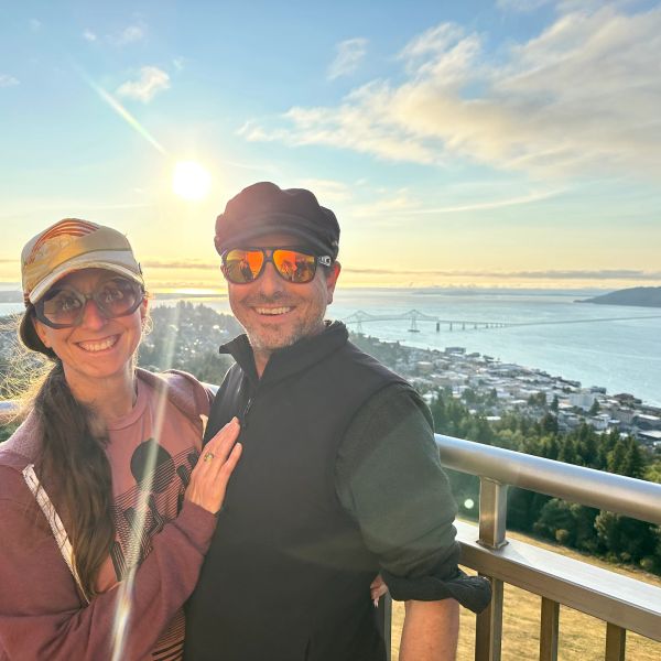 Happy couple posing with a scenic waterfront and bridge at sunset.
