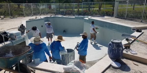 Workers renovating an empty swimming pool outdoors.