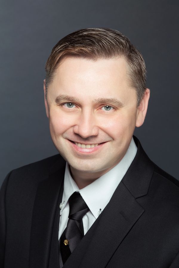 Professional man in a suit smiling against a dark background.