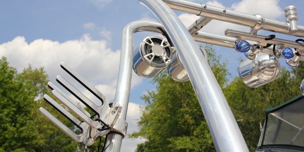Close-up of a boat's wakeboard tower with speakers and lights under a partly cloudy sky.
