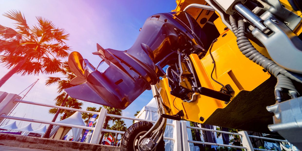 Close-up of a boat's outboard motor and wheel against a sunny sky.