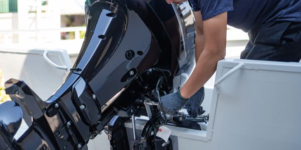 Man repairing a black boat engine on a white boat.