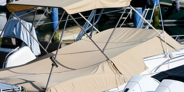 A beige-covered motorboat docked at a marina with other boats in the background.
