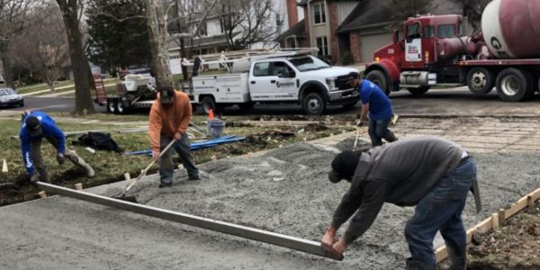 Workers pouring and leveling concrete on a driveway.