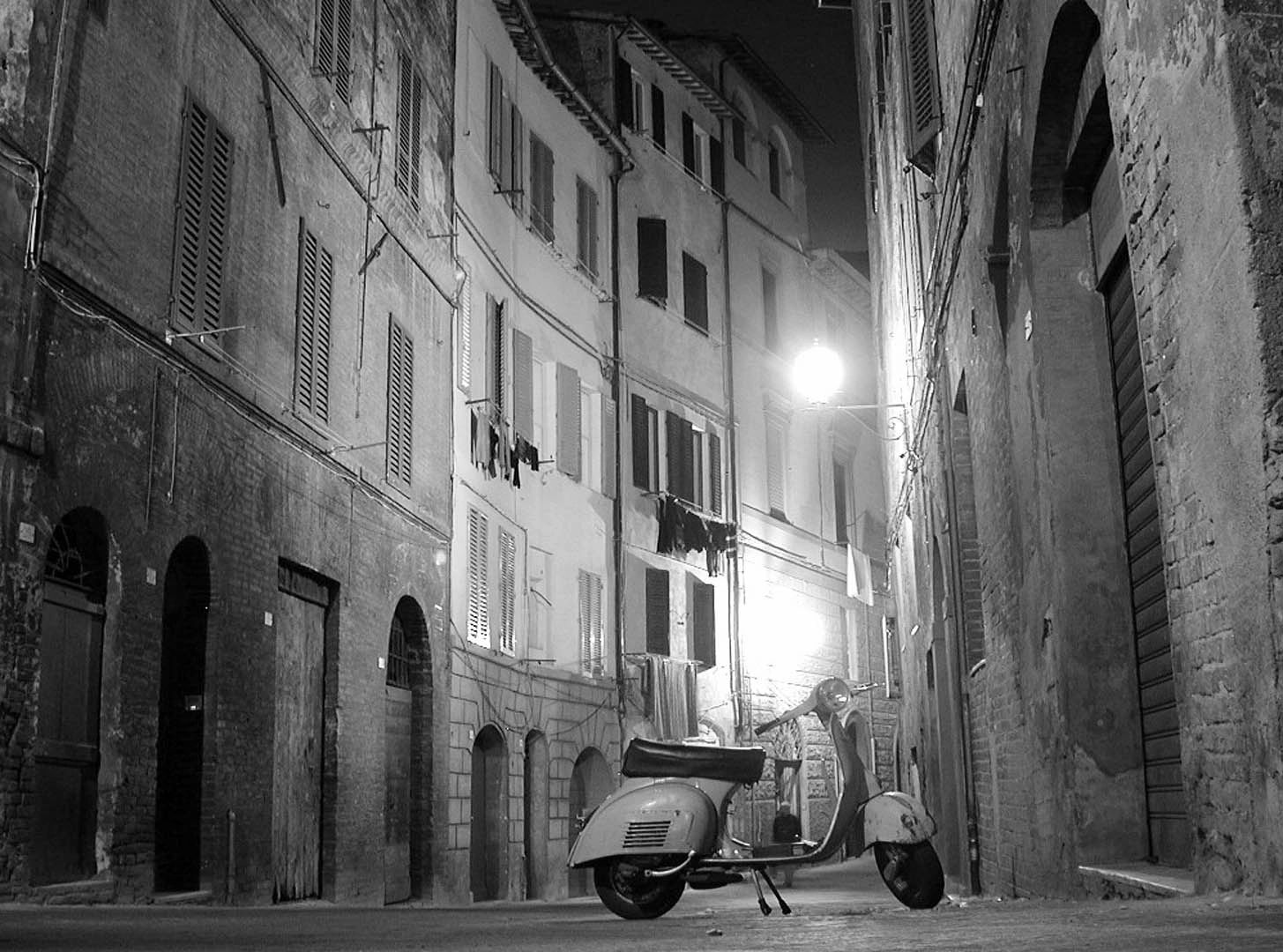 Vintage scooter parked on a narrow, dimly lit European street at night.